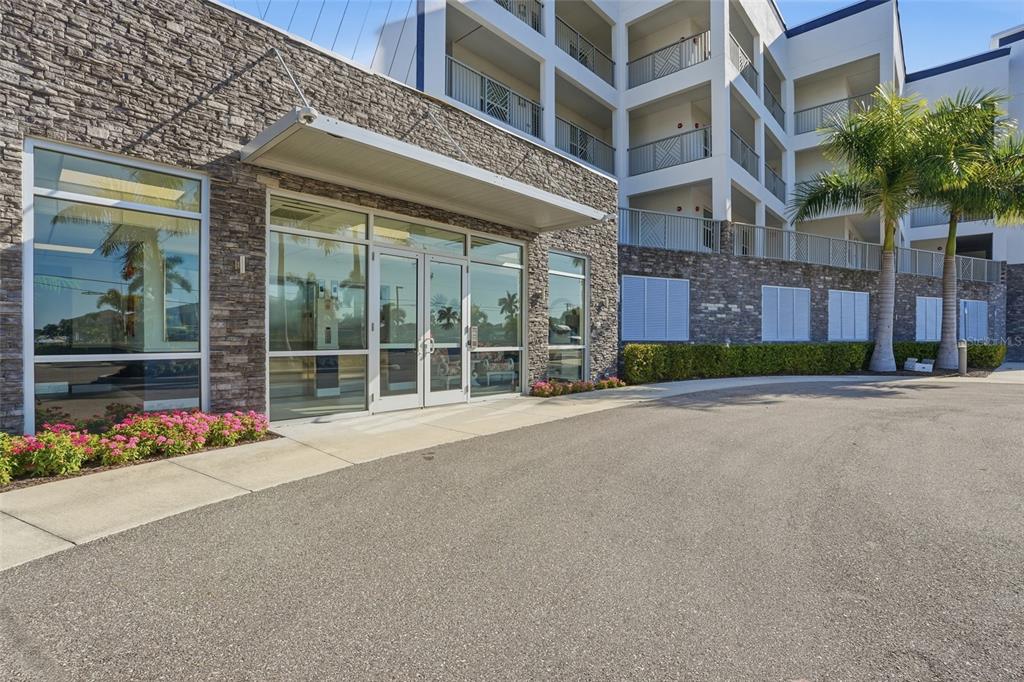 A stone-faced building exterior features a glass entrance with a metal awning and palm trees — 1425 PARK BEACH CIRCLE UNIT 124, PUNTA GORDA, FL