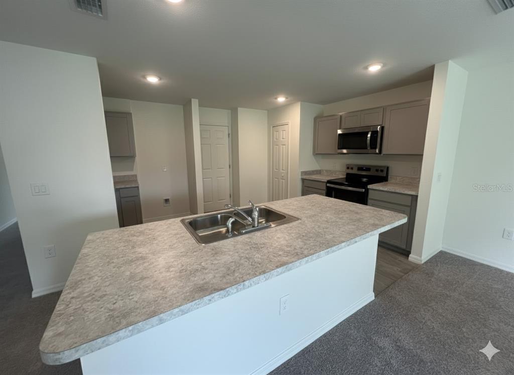 A kitchen features a central island with a sink, grey cabinets, and carpeted flooring — 2116 HANSON STREET, PORT CHARLOTTE, FL
