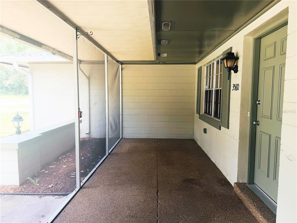A covered concrete porch features a screened-in side, a green front door, and block walls — 3560 SW 150TH LANE ROAD, OCALA, FL