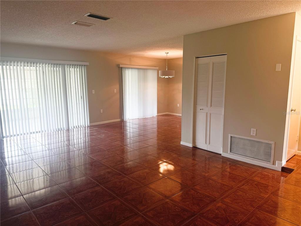 An open-concept living and dining area features glossy brown tile flooring and vertical window blinds — 3560 SW 150TH LANE ROAD, OCALA, FL