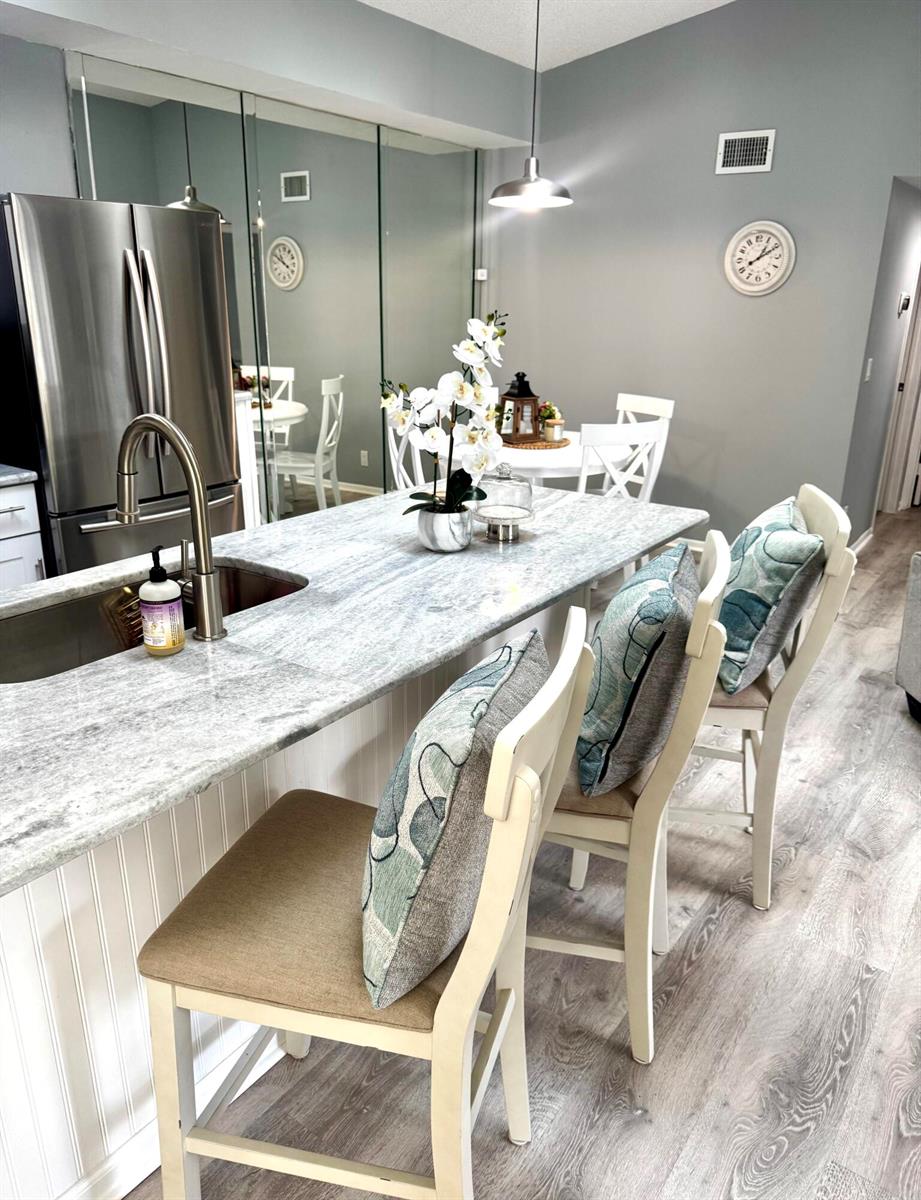 A kitchen island with a stone countertop and three bar stools sits before a dining area — 2502 SE Anchorage Cove # 3, FL 34952, FL