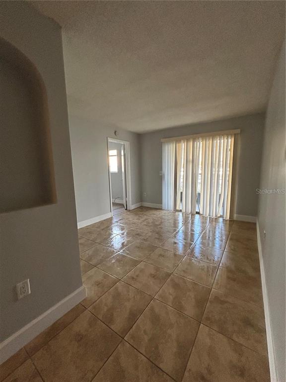 An empty room with light gray walls, tan tile flooring, and vertical blinds over sliding doors — 946 LAKE DESTINY ROAD UNIT D, ALTAMONTE SPRINGS, FL