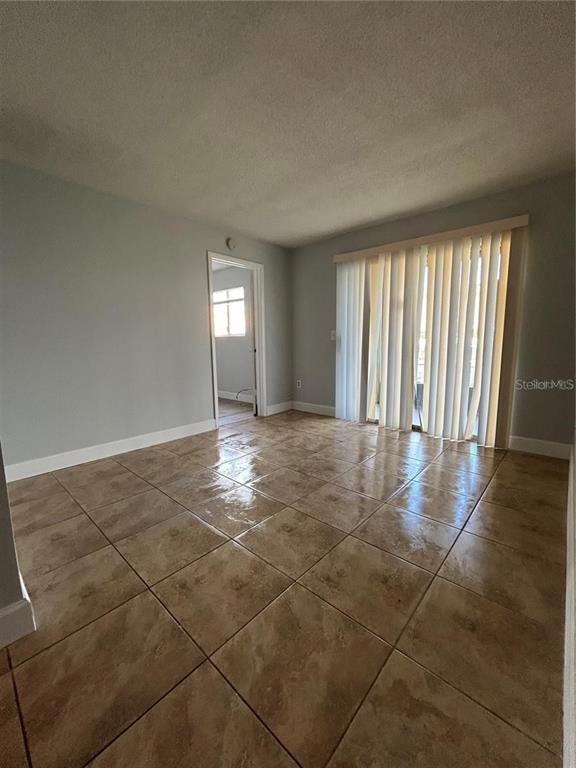 An empty room features light gray walls, tan tile flooring, and vertical blinds over sliding doors — 946 LAKE DESTINY ROAD UNIT D, ALTAMONTE SPRINGS, FL
