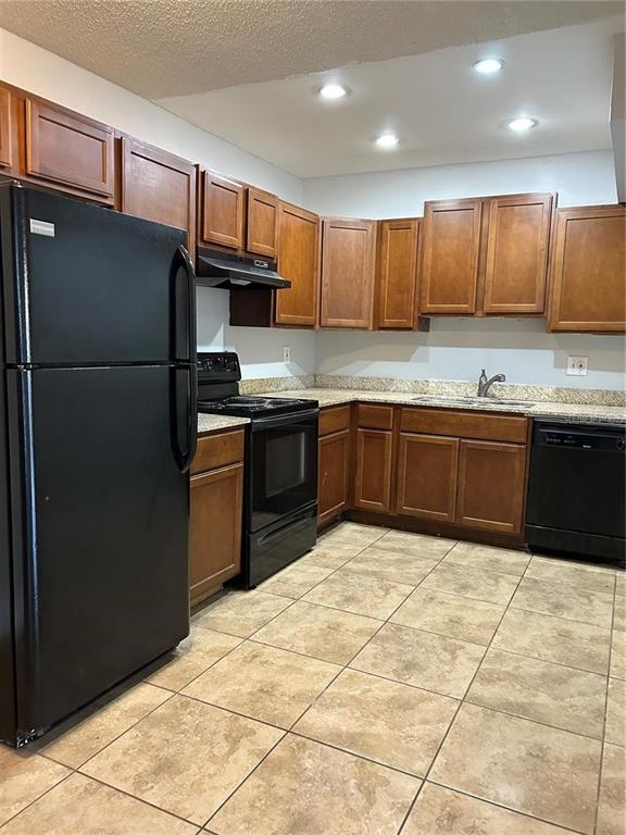 A kitchen features wood cabinets, black appliances, granite countertops, and light-colored tile flooring — 946 LAKE DESTINY ROAD UNIT D, ALTAMONTE SPRINGS, FL