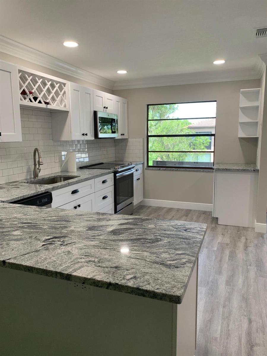A kitchen with white cabinets, granite countertops, stainless steel appliances, and light wood-look flooring — 9199 Pecky Cypress Lane # 7d, Boca Raton FL 33428, BOCA RATON, FL