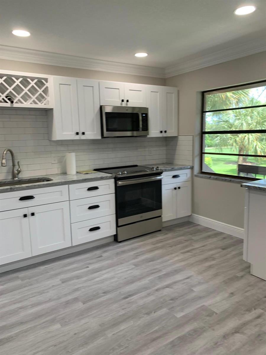 A kitchen with white cabinets, stainless steel appliances, gray countertops, and light wood-look flooring — 9199 Pecky Cypress Lane # 7d, Boca Raton FL 33428, BOCA RATON, FL