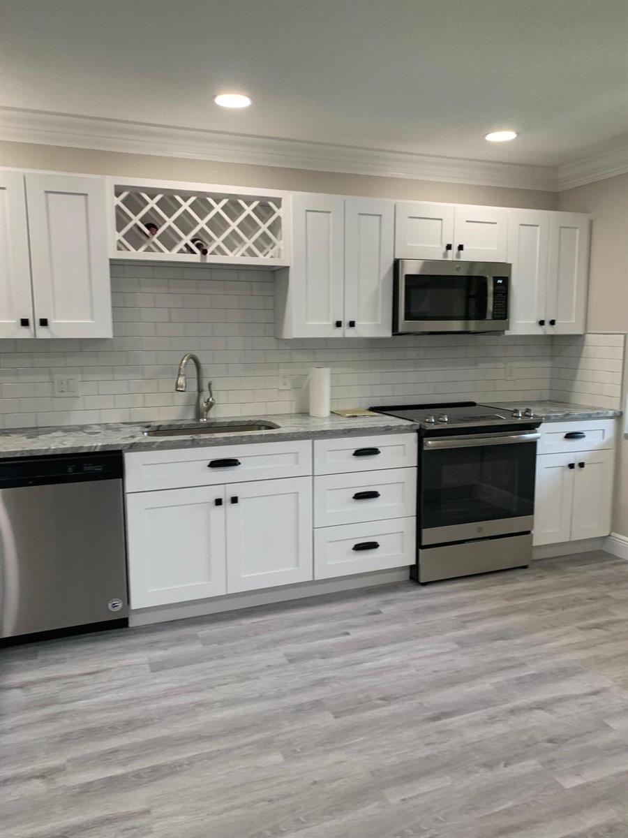 A kitchen features white cabinets, stainless steel appliances, a gray countertop, and light wood flooring — 9199 Pecky Cypress Lane # 7d, Boca Raton FL 33428, BOCA RATON, FL