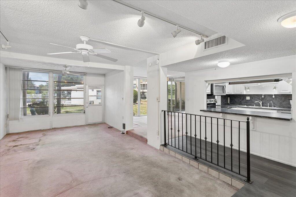 A living room with pink carpet, a ceiling fan, and an open kitchen pass-through window — 9491 Evergreen Place # 108, Davie FL 33324, DAVIE, FL