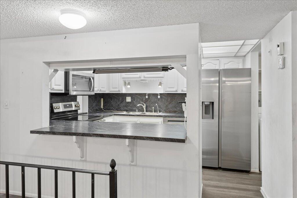 A kitchen with a pass-through window, dark countertops, white cabinets, and stainless steel appliances — 9491 Evergreen Place # 108, Davie FL 33324, DAVIE, FL