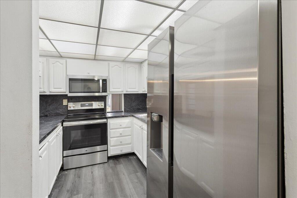A kitchen features white cabinets, stainless steel appliances, and dark countertops with gray flooring — 9491 Evergreen Place # 108, Davie FL 33324, DAVIE, FL