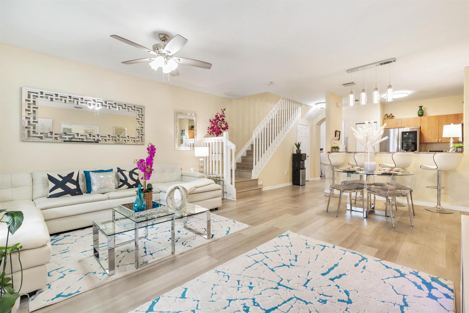 An open-concept living and dining area features a white sectional sofa, stairs, and kitchen — 3725 Oleander Terrace, Riviera Beach FL 33404, RIVIERA BEACH, FL