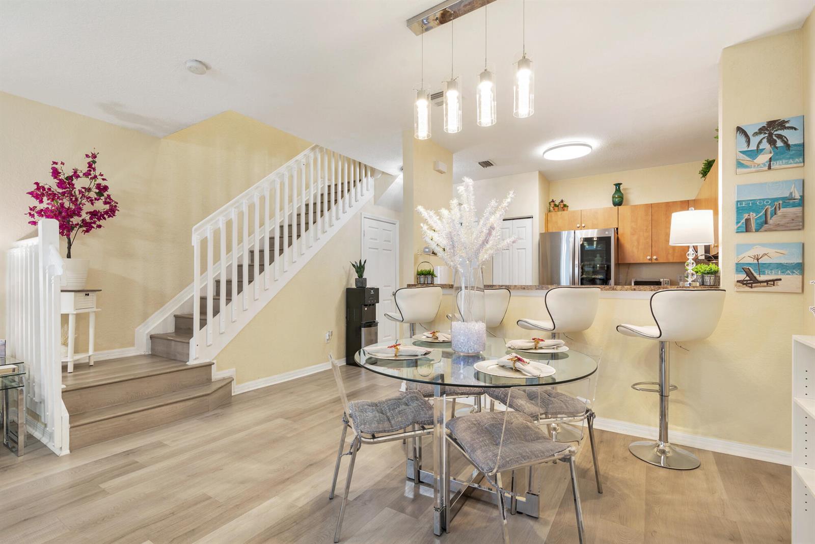 A dining area with a glass table, bar stools, and a staircase with white railings — 3725 Oleander Terrace, Riviera Beach FL 33404, RIVIERA BEACH, FL