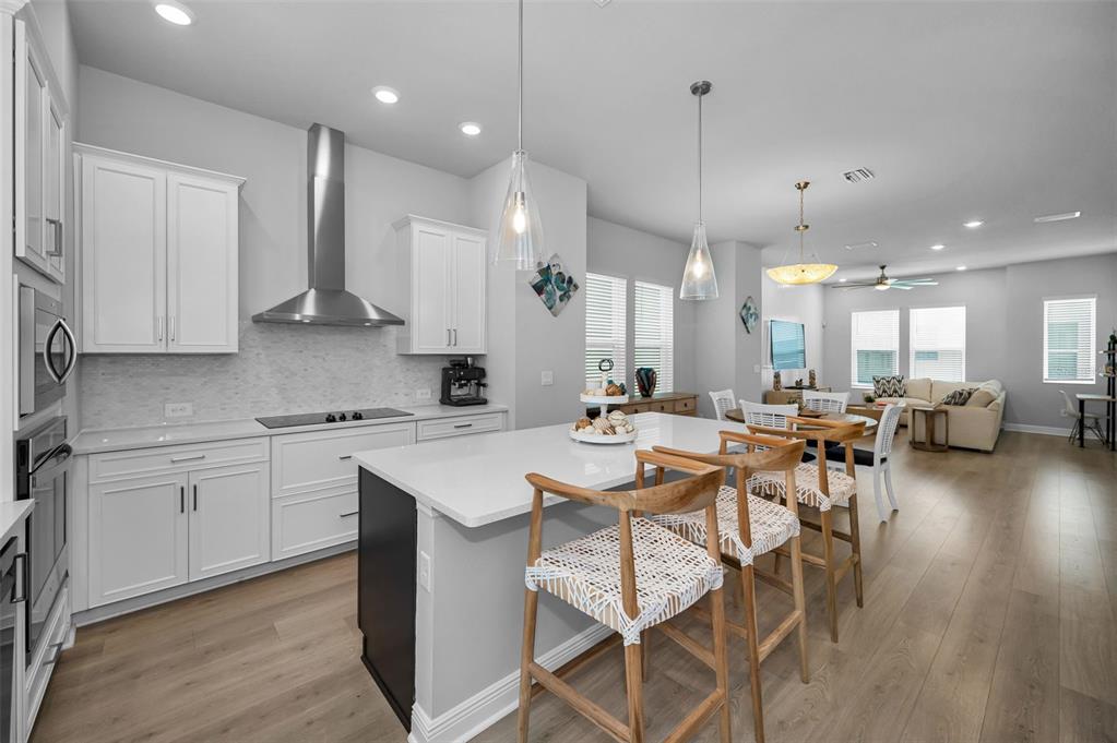 A modern kitchen with white cabinets, a large island, and wood flooring opens to a living area — 2458 MANGUM COURT, SARASOTA, FL