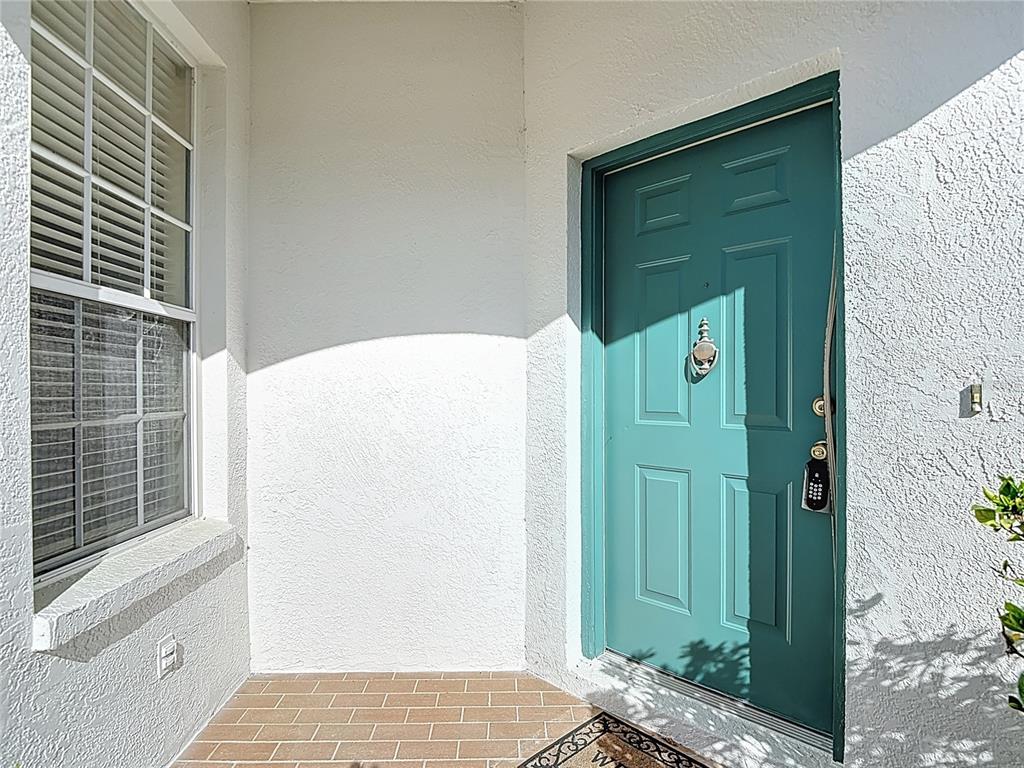 A teal front door with a silver knocker sits beside a window on a porch — 1931 SASSAFRAS DRIVE, WESLEY CHAPEL, FL