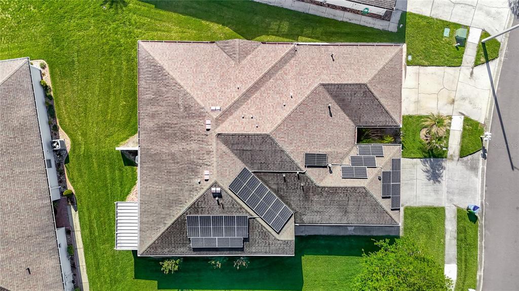 An aerial view shows a residential house roof with solar panels and surrounding green lawns — 1931 SASSAFRAS DRIVE, WESLEY CHAPEL, FL