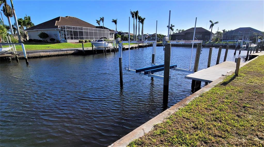A canal view shows a boat lift, a concrete dock, and residential houses in the background — 1418 SEA GULL COURT, PUNTA GORDA, FL