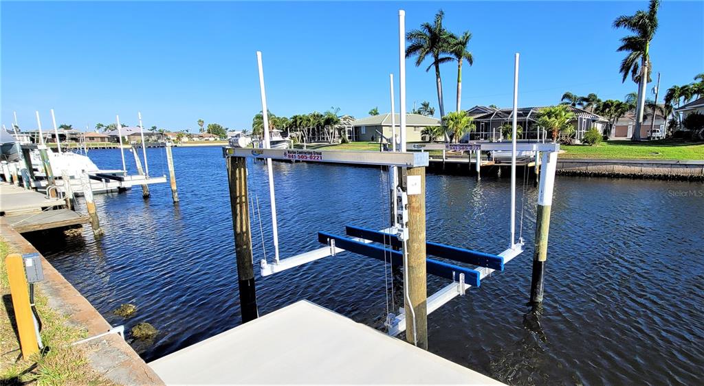 A boat lift sits in a canal next to a concrete dock and residential homes — 1418 SEA GULL COURT, PUNTA GORDA, FL