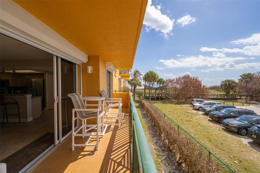 A balcony with patio furniture overlooks a parking lot and a beach area with trees — 8472 RIDGEWOOD AVENUE UNIT 201, CAPE CANAVERAL, FL