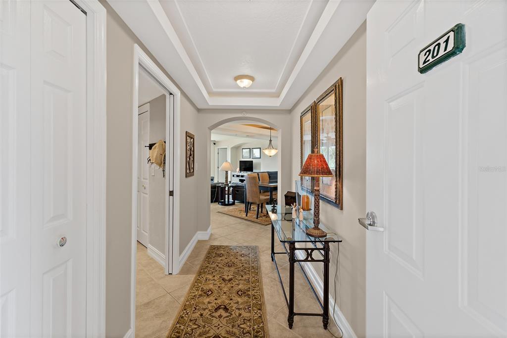 A hallway with tile floors, a runner rug, and a console table leads to a living area — 8472 RIDGEWOOD AVENUE UNIT 201, CAPE CANAVERAL, FL