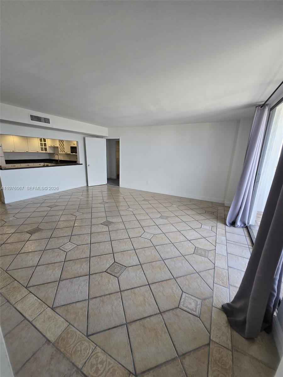 An open living area features beige tile flooring, a kitchen pass-through, and sliding glass doors — 13499 Biscayne Blvd # 1505, North Miami FL 33181, NORTH MIAMI, FL