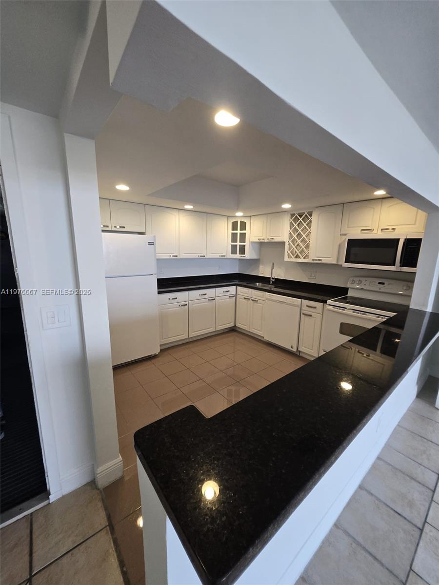 A kitchen features white cabinets, black countertops, and light-colored tile flooring — 13499 Biscayne Blvd # 1505, North Miami FL 33181, NORTH MIAMI, FL