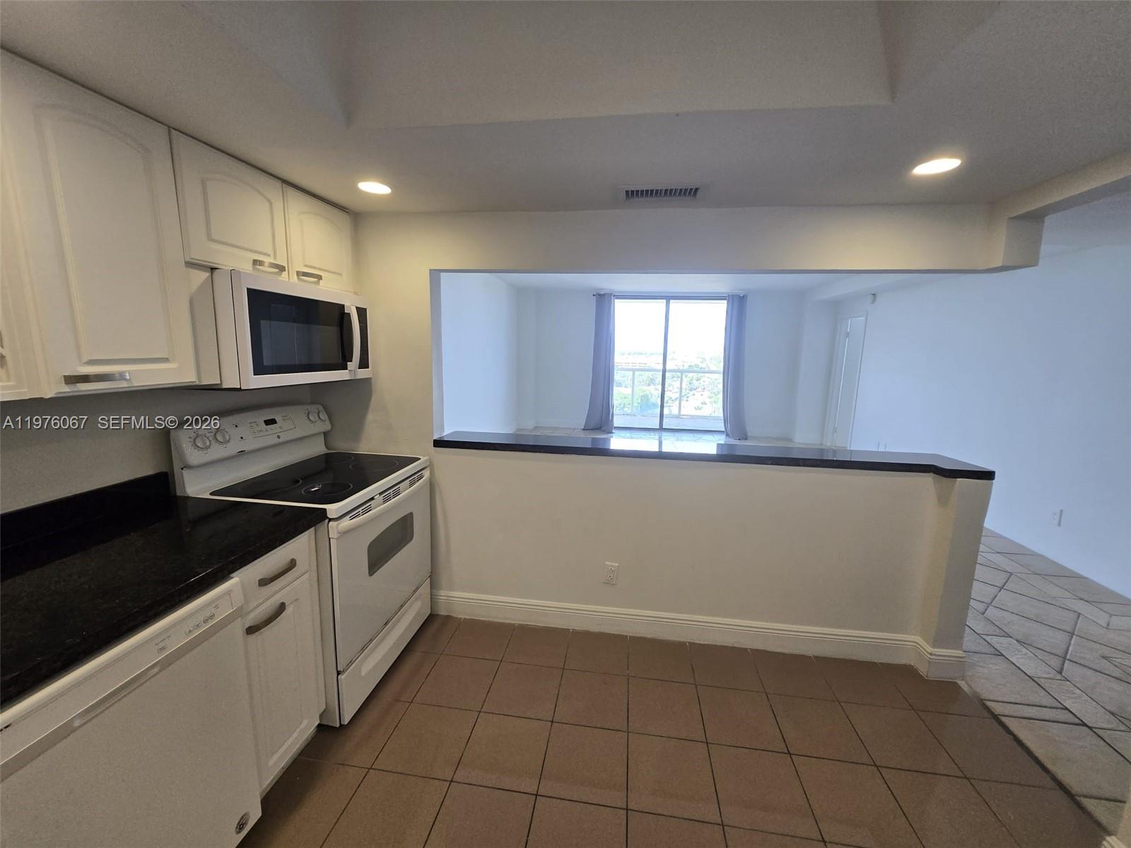 A kitchen with white cabinets, black countertops, and a pass-through window to the living area — 13499 Biscayne Blvd # 1505, North Miami FL 33181, NORTH MIAMI, FL