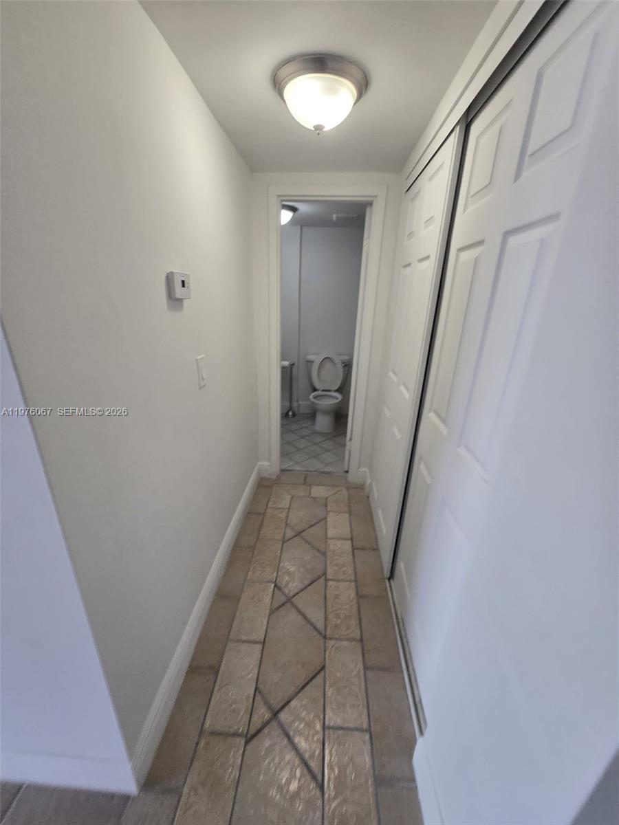 A tiled hallway leads to a bathroom with a toilet and a light fixture — 13499 Biscayne Blvd # 1505, North Miami FL 33181, NORTH MIAMI, FL