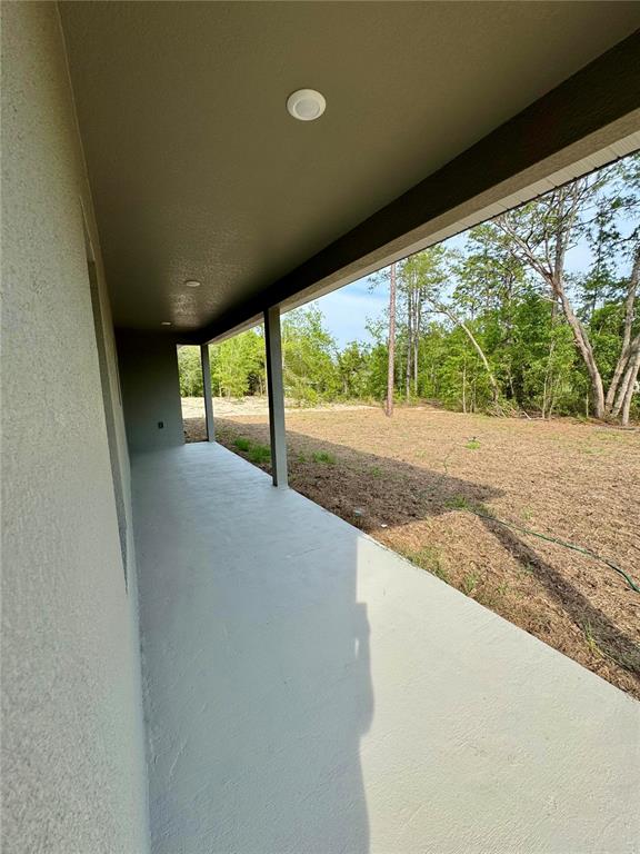 A covered concrete patio overlooks a grassy backyard with trees under a clear sky — 152 W DIEGO PLACE, CITRUS SPRINGS, FL
