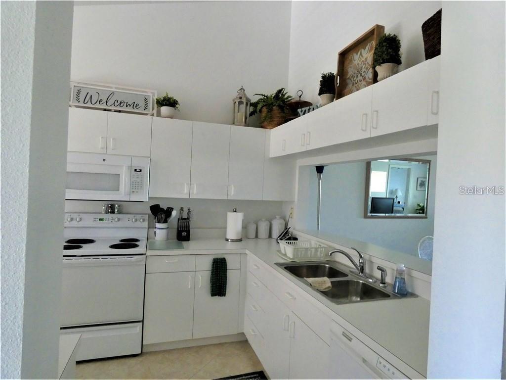 A kitchen features white cabinets, white appliances, and a pass-through window to another room — 8735 OLDE HICKORY AVENUE UNIT 8302, SARASOTA, FL