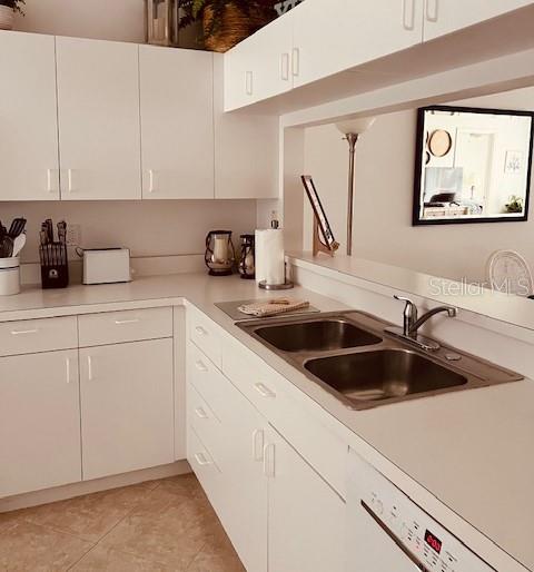A white kitchen features a double-basin sink, white cabinetry, and a pass-through window with mirror — 8735 OLDE HICKORY AVENUE UNIT 8302, SARASOTA, FL