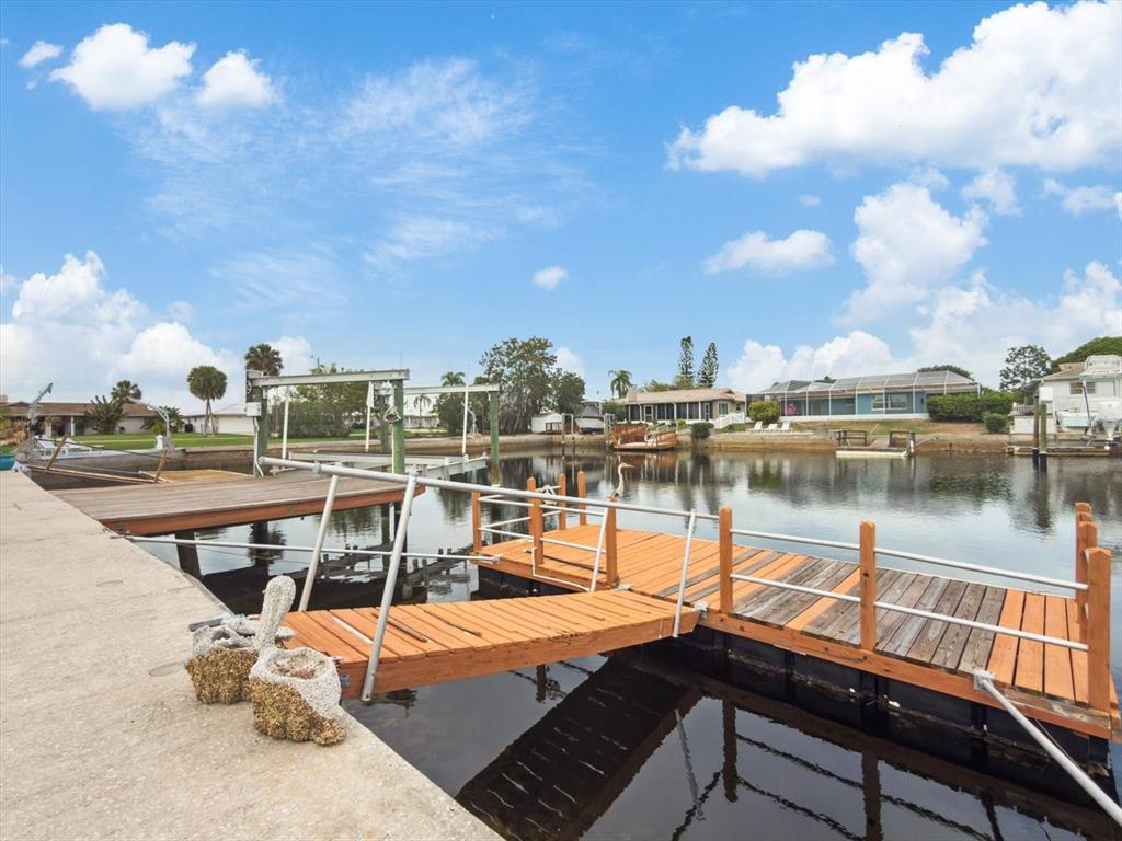 A wooden floating dock extends into a calm canal with houses in the background — 5008 DORY DRIVE, NEW PORT RICHEY, FL