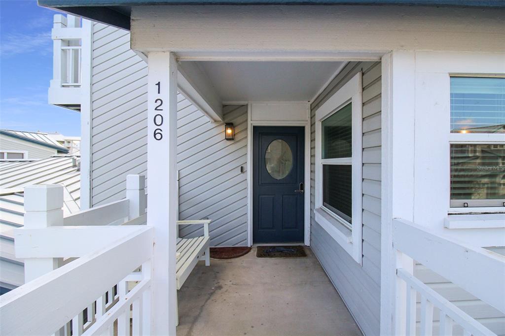 A covered entryway features a dark blue front door, light gray siding, and a white bench — 1206 SIESTA BAYSIDE DRIVE UNIT 1206B, SARASOTA, FL