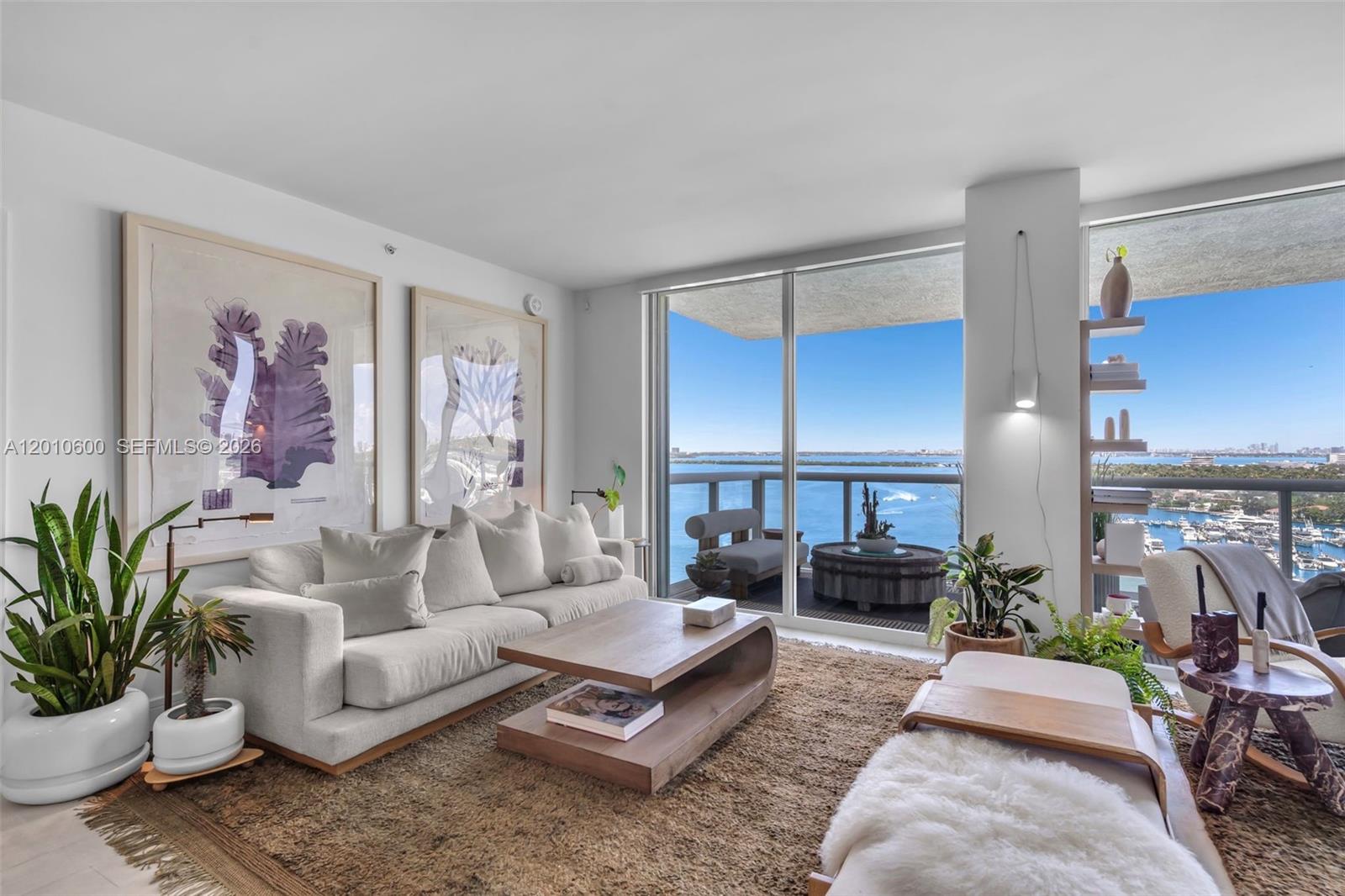 A living room features a beige sofa, wooden coffee table, and balcony with water views — 10 Venetian Way # 1803, Miami Beach FL 33139, MIAMI BEACH, FL