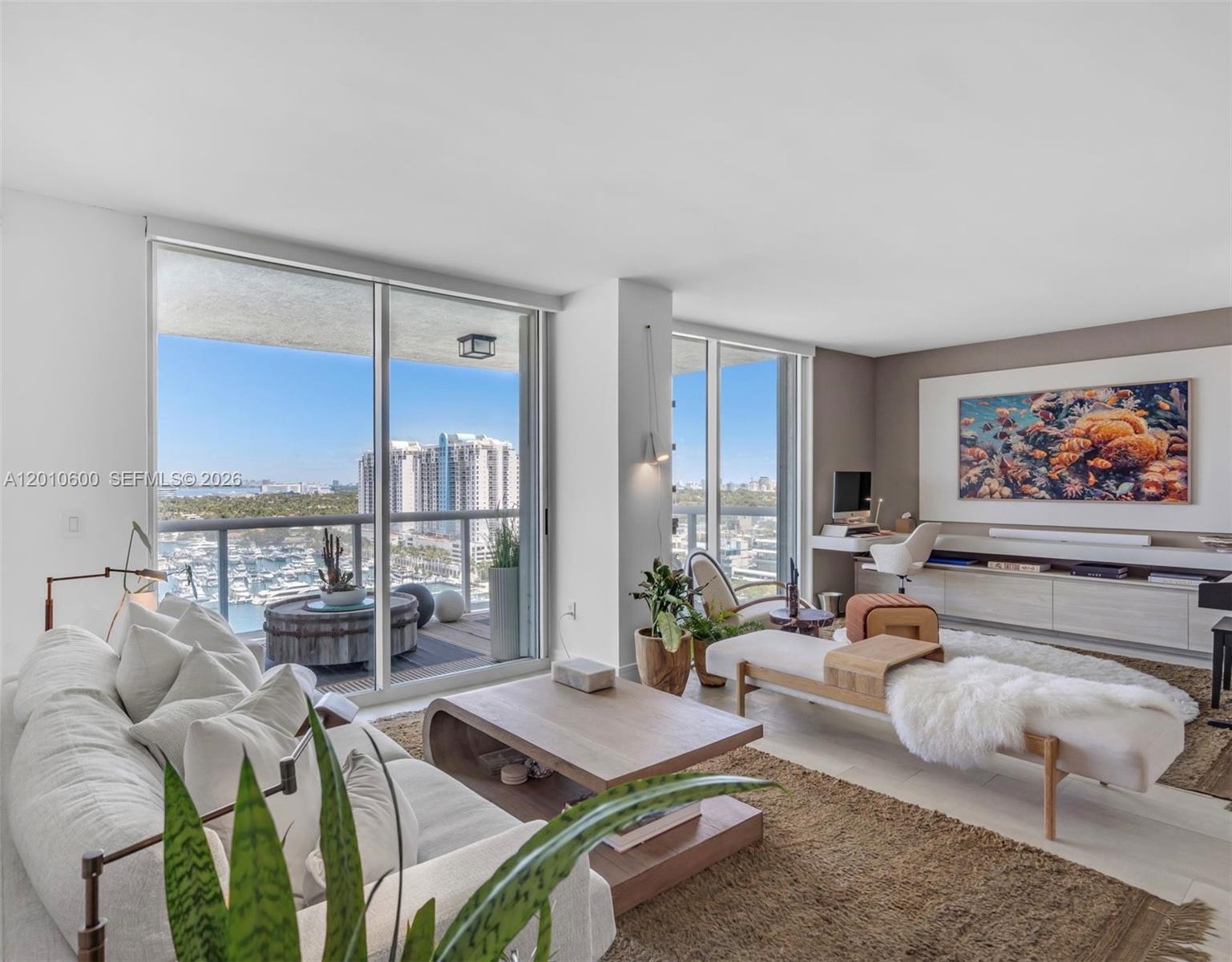 A modern living room features a sofa, wooden coffee table, and floor-to-ceiling windows overlooking a marina — 10 Venetian Way # 1803, Miami Beach FL 33139, MIAMI BEACH, FL