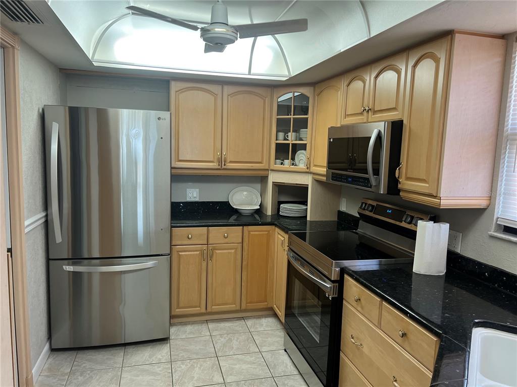 A kitchen features light wood cabinets, black countertops, stainless steel appliances, and tiled flooring — 4260 SE 20TH PLACE UNIT 801, CAPE CORAL, FL