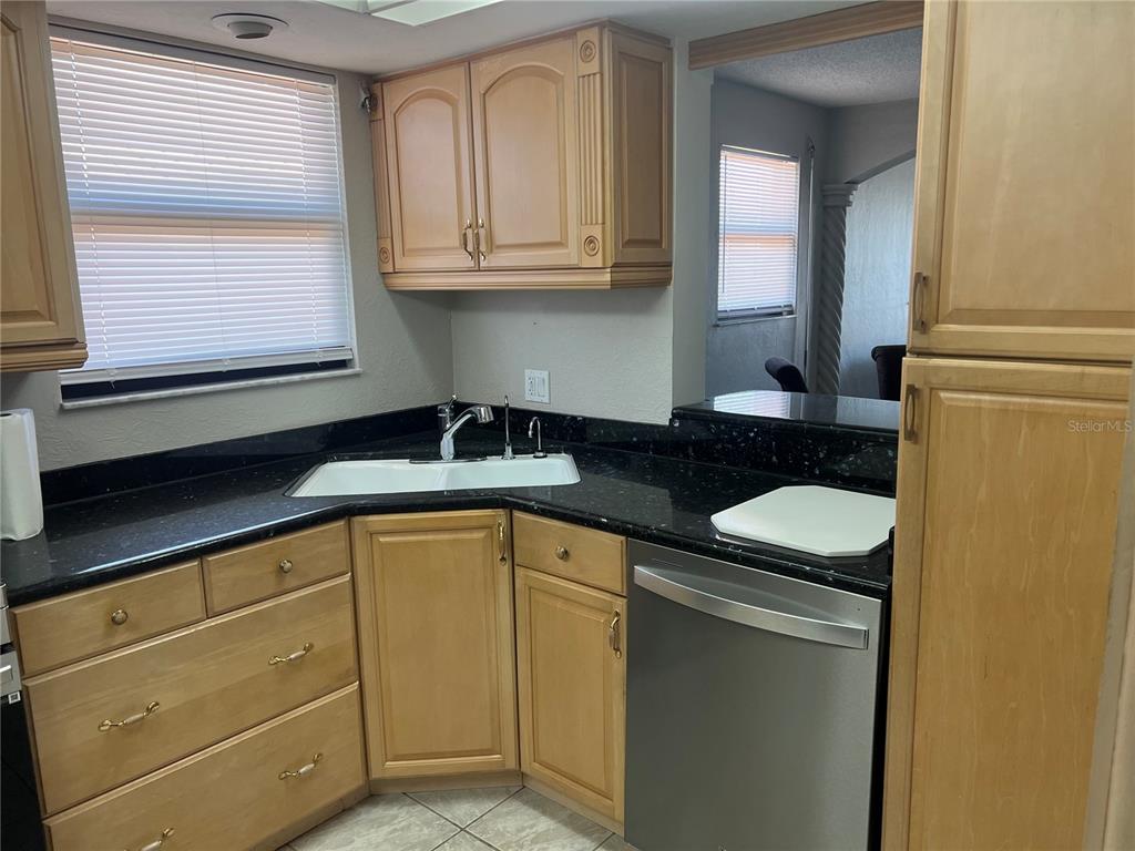 A kitchen features light wood cabinets, black countertops, a corner sink, and stainless steel appliances — 4260 SE 20TH PLACE UNIT 801, CAPE CORAL, FL