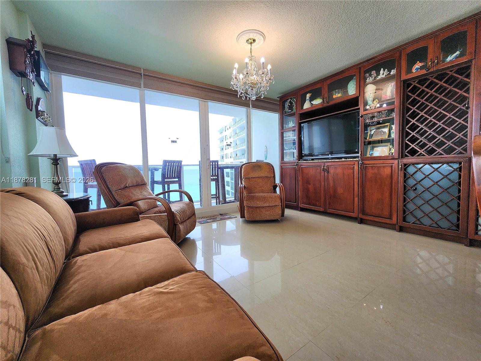 A living room features a brown sofa, two recliners, a large wooden wall unit, and balcony access — 3505 S Ocean Dr # 1006, Hollywood FL 33019, HOLLYWOOD, FL