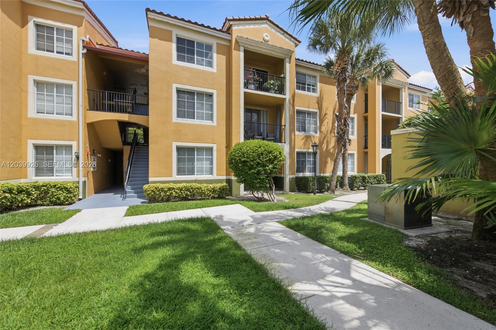 A three-story apartment building with yellow stucco walls, balconies, and a concrete walkway — 2351 W Preserve Way # 306, Miramar FL 33025, MIRAMAR, FL
