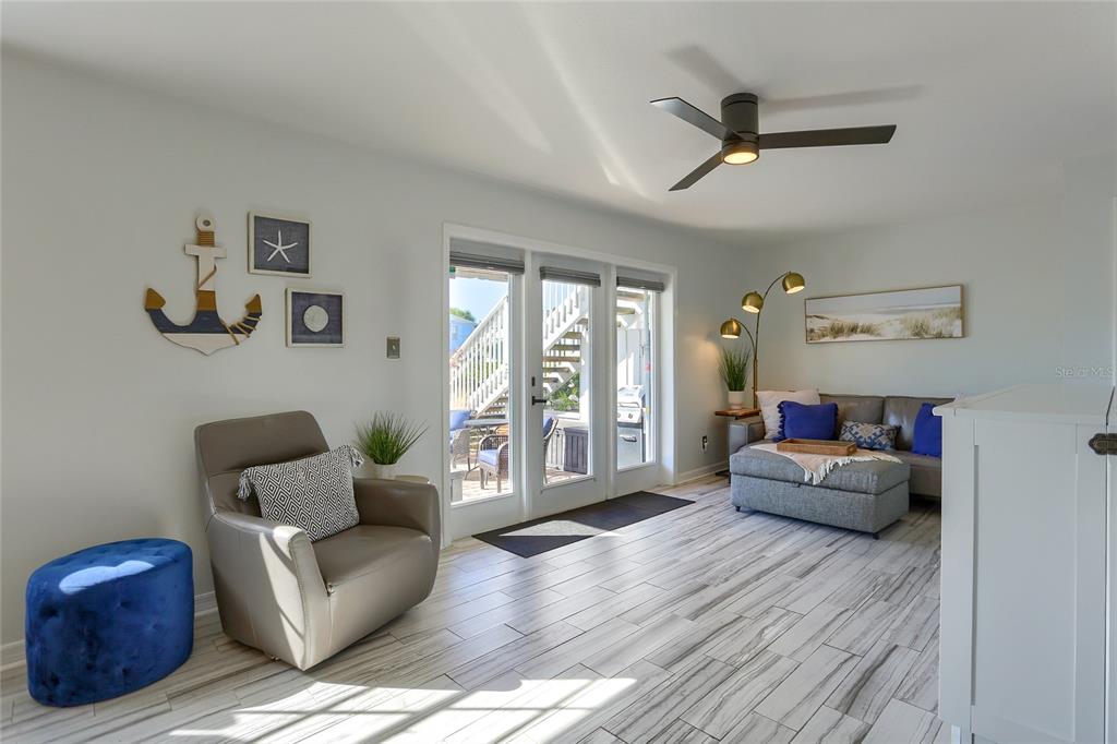 A living room features light wood-look tile flooring, a gray armchair, and a sectional sofa — 4975 COBIA DRIVE SE UNIT A, ST PETERSBURG, FL