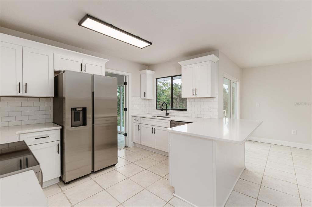 A kitchen with white cabinets, stainless steel appliances, a white island, and light tile flooring — 4826 KIMBALL COURT W, LAKELAND, FL
