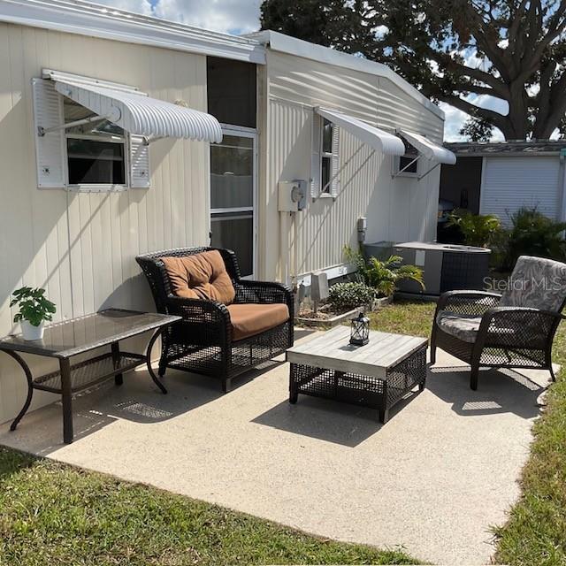 A patio with wicker furniture sits outside a mobile home with metal window awnings — 72 PINDO PALM STREET W, LARGO, FL