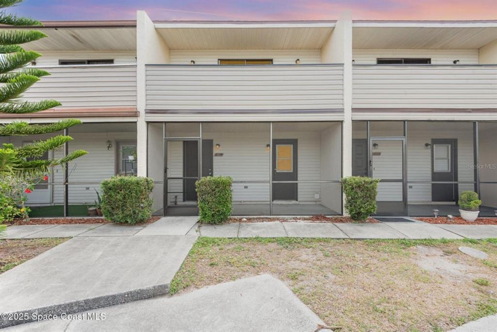 A row of townhouses features screened-in front porches, light-colored siding, and concrete walkways — 3164 FINSTERWALD DRIVE UNIT 3164, TITUSVILLE, FL
