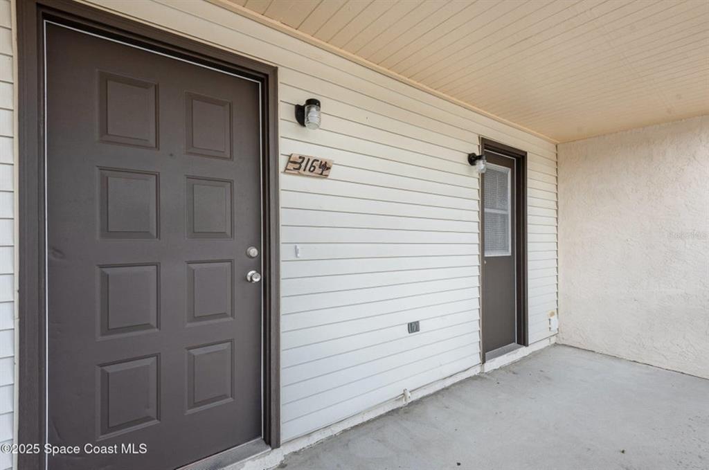 A covered porch features a brown front door, a side door, and white siding — 3164 FINSTERWALD DRIVE UNIT 3164, TITUSVILLE, FL