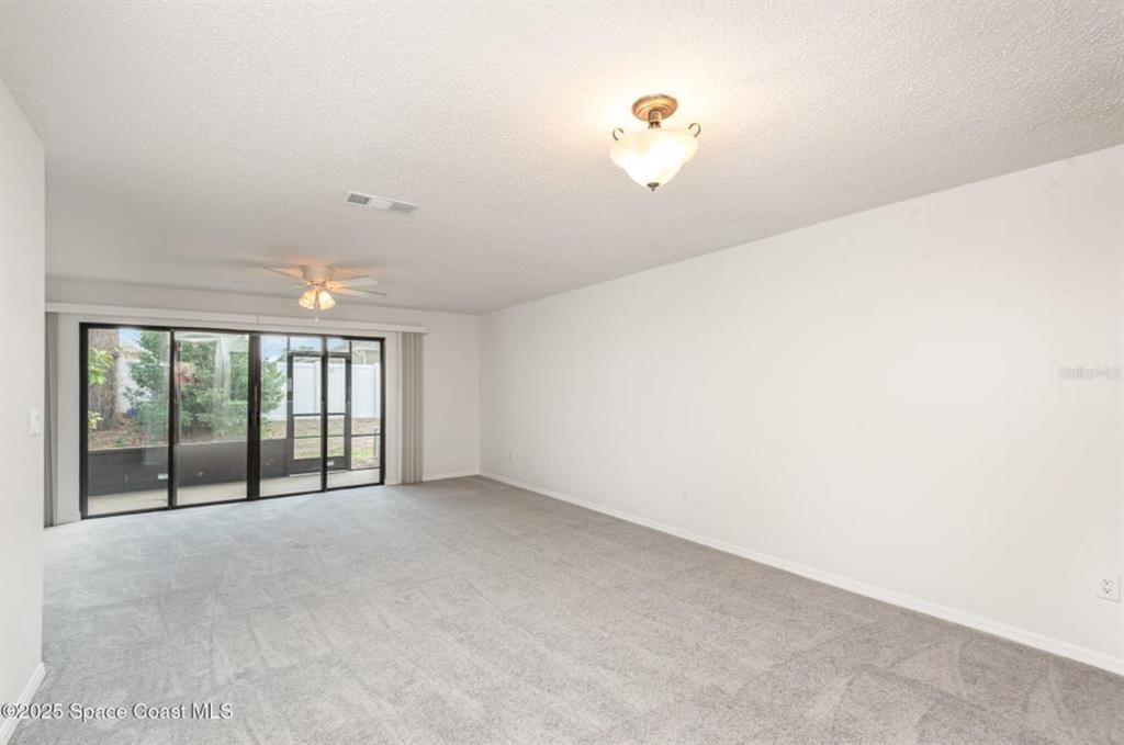 A carpeted living room features a ceiling fan, a light fixture, and sliding glass doors — 3164 FINSTERWALD DRIVE UNIT 3164, TITUSVILLE, FL