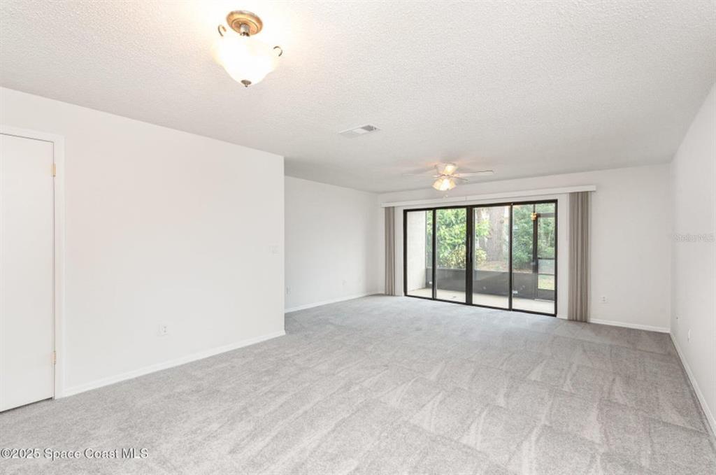 A living room with gray carpet, white walls, a ceiling fan, and sliding glass doors — 3164 FINSTERWALD DRIVE UNIT 3164, TITUSVILLE, FL