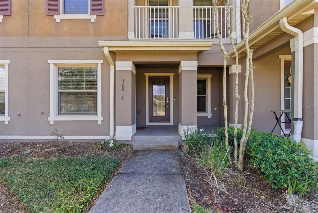 A concrete walkway leads to the covered front entrance of a two-story tan stucco home — 10814 SUNSET RIDGE LANE, ORLANDO, FL