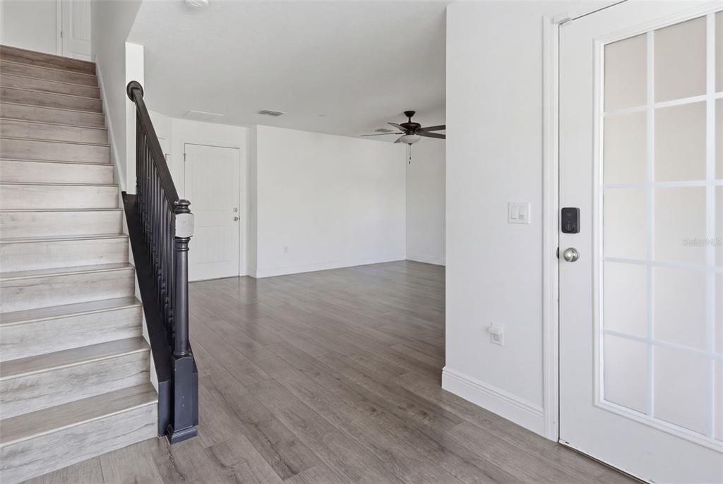 An entryway features light wood-look flooring, a staircase with a black railing, and white walls — 10814 SUNSET RIDGE LANE, ORLANDO, FL