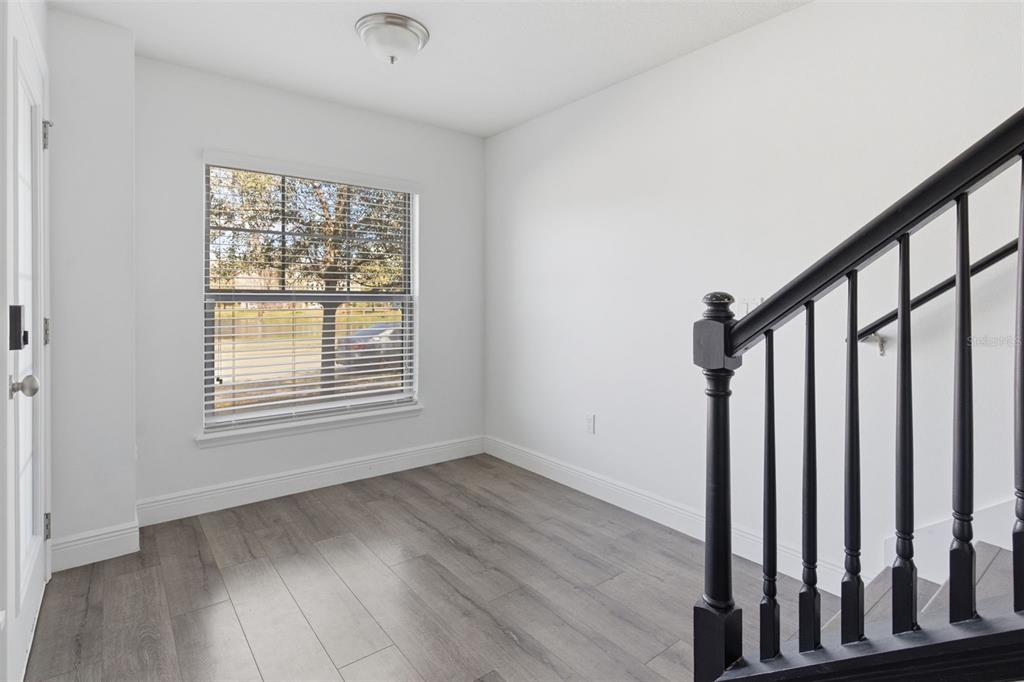 An empty room with gray wood-look flooring, white walls, a window, and a black staircase railing — 10814 SUNSET RIDGE LANE, ORLANDO, FL