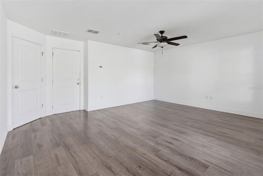 An empty room features white walls, a ceiling fan, and gray wood-look flooring — 10814 SUNSET RIDGE LANE, ORLANDO, FL
