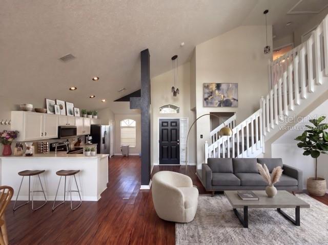 An open-concept living room and kitchen feature dark wood floors, white cabinetry, and a staircase — 8103 TAR HOLLOW DRIVE, GIBSONTON, FL